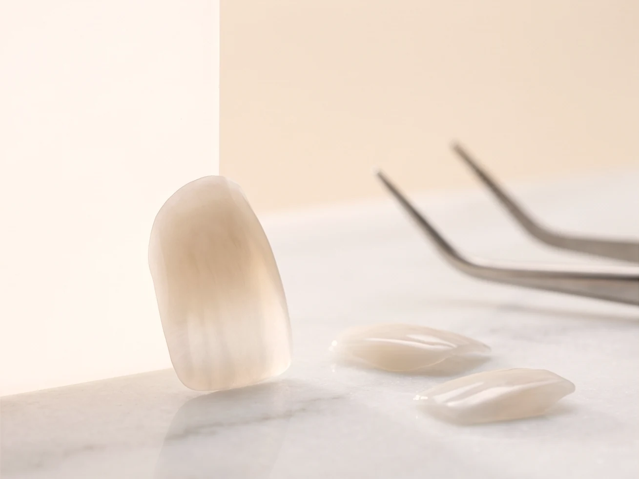 Laminados cerâmicos ultrafinos sobre superfície de mármore, um deles em pé mostrando a translucidez.